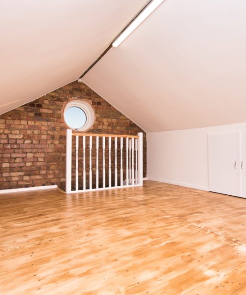 Bright attic room featuring wooden flooring, a circular window, and a white railing, ideal for various uses.