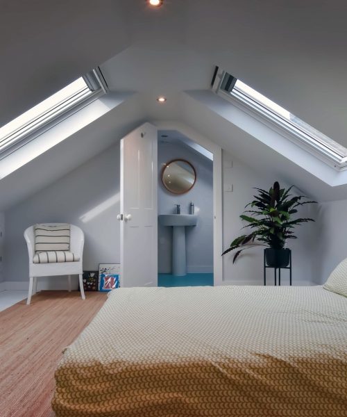 Cozy attic bedroom featuring a bed, skylights, and a plant, designed for relaxation and comfort in a modern home.